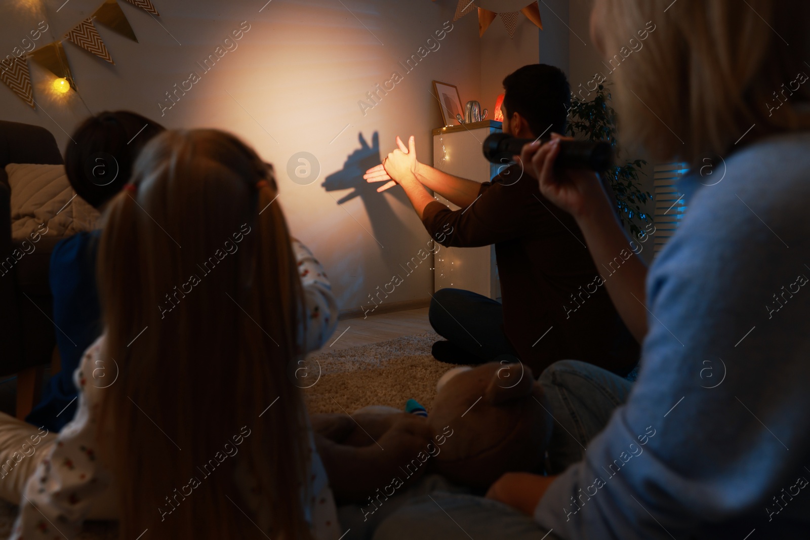 Photo of Man making hand gesture like donkey while performing shadow play to his family at home