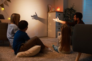 Photo of Man making hand gesture like dog while performing shadow play to his family at home