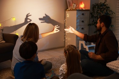 Photo of Parents making hand gestures like bunny and dog while performing shadow play to their kids at home