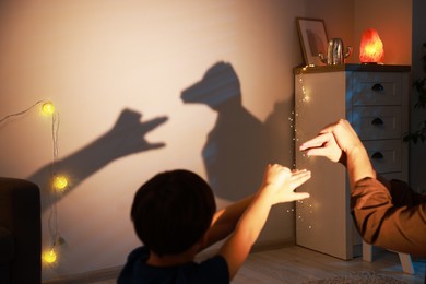 Photo of Shadow play. Father with his son making hand gestures like goose and duck on wall at home, closeup