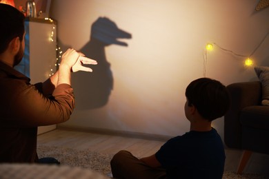 Photo of Father making hand gesture like duck while performing shadow play to his son at home