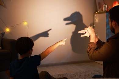 Photo of Father making hand gesture like duck while performing shadow play to his son at home