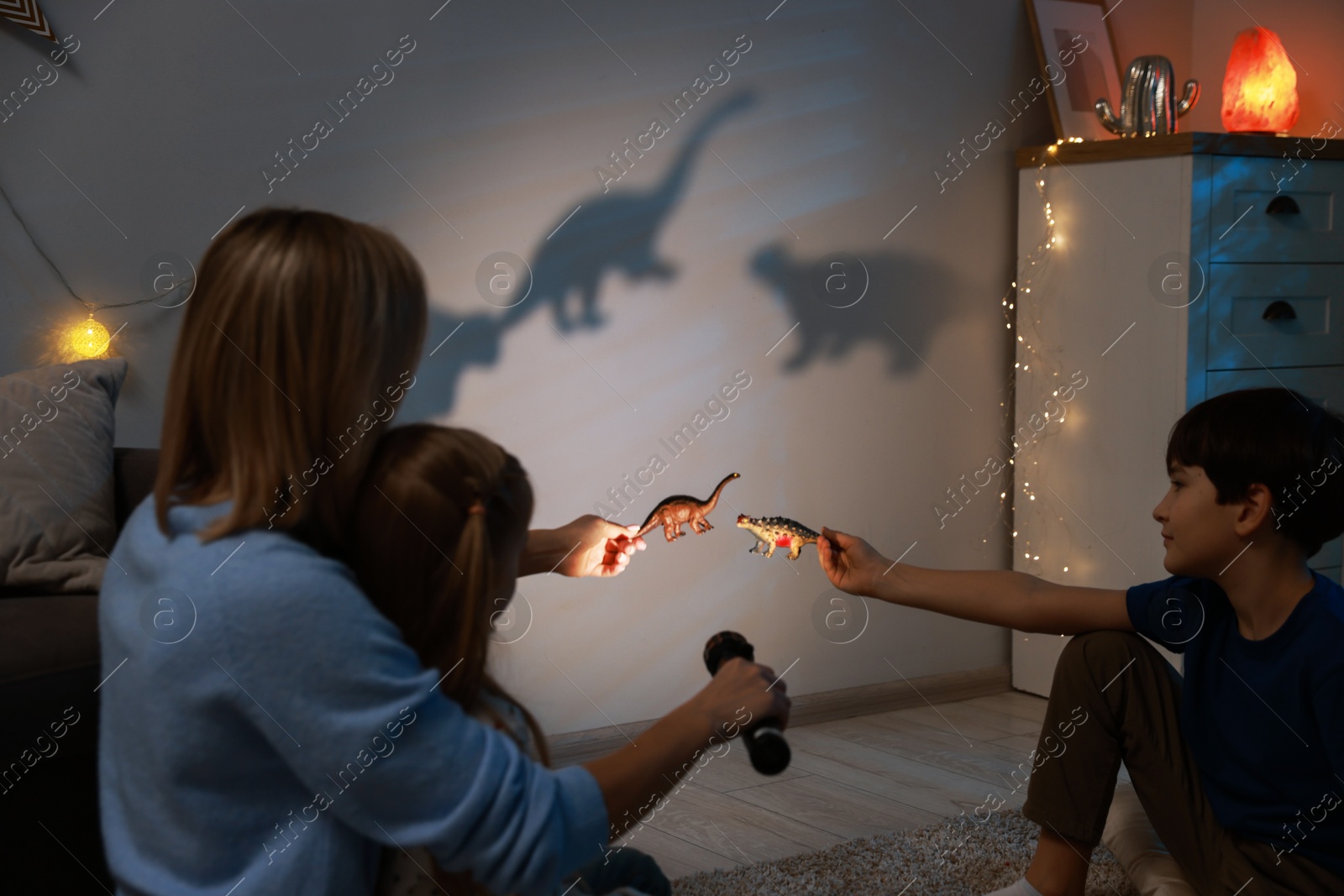 Photo of Mother and her son performing shadow play with toy dinosaurs at home