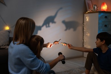 Photo of Mother and her son performing shadow play with toy dinosaurs at home