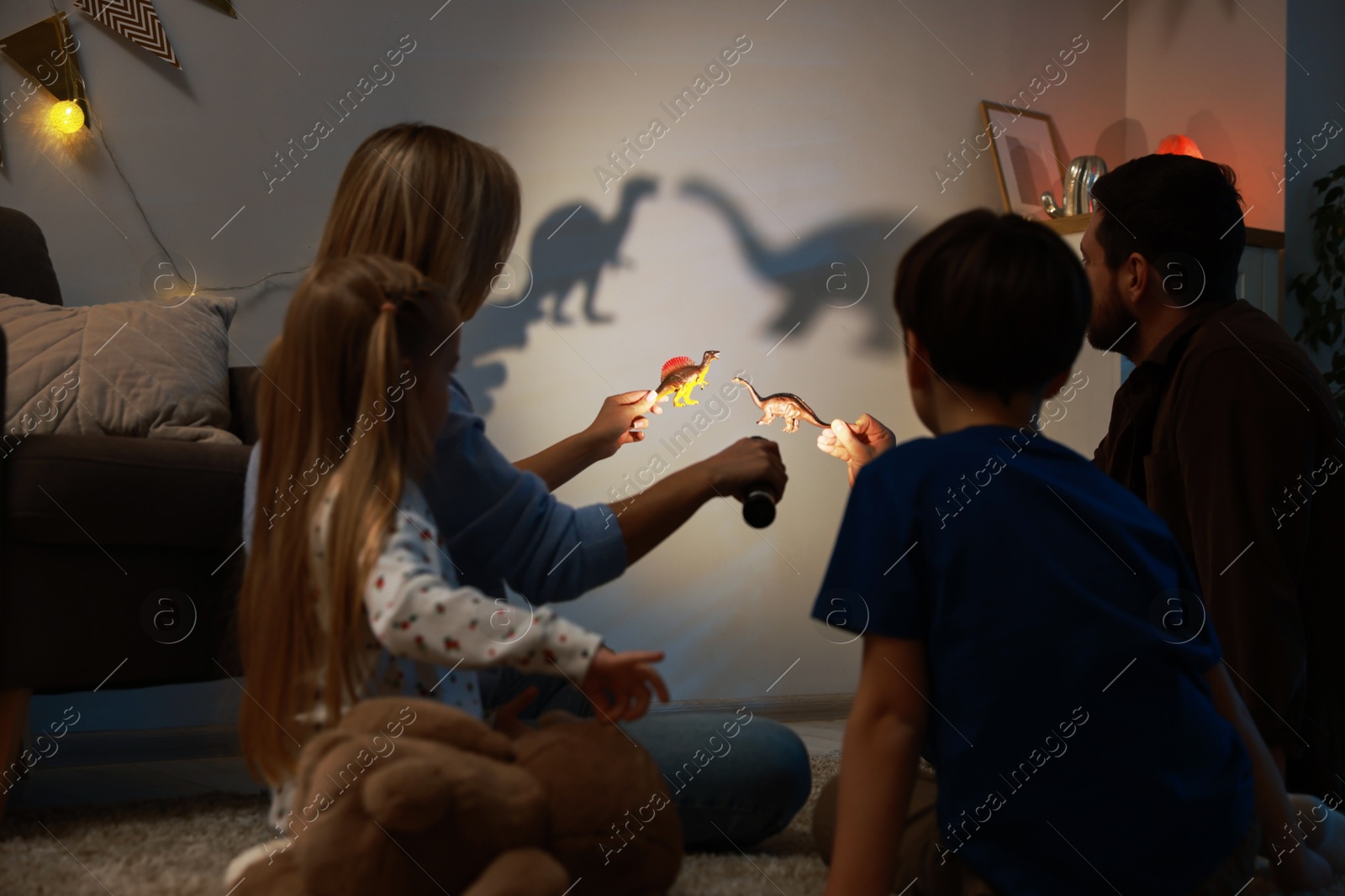 Photo of Parents performing shadow play with toy dinosaurs to their kids at home