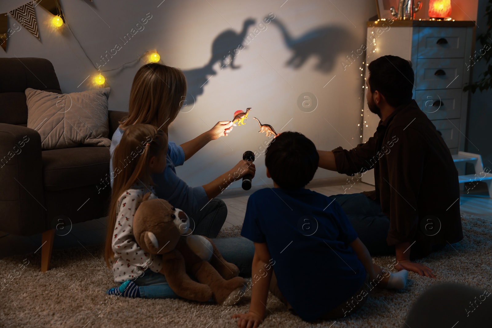 Photo of Parents performing shadow play with toy dinosaurs to their kids at home