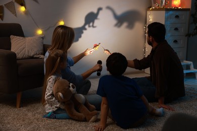 Parents performing shadow play with toy dinosaurs to their kids at home