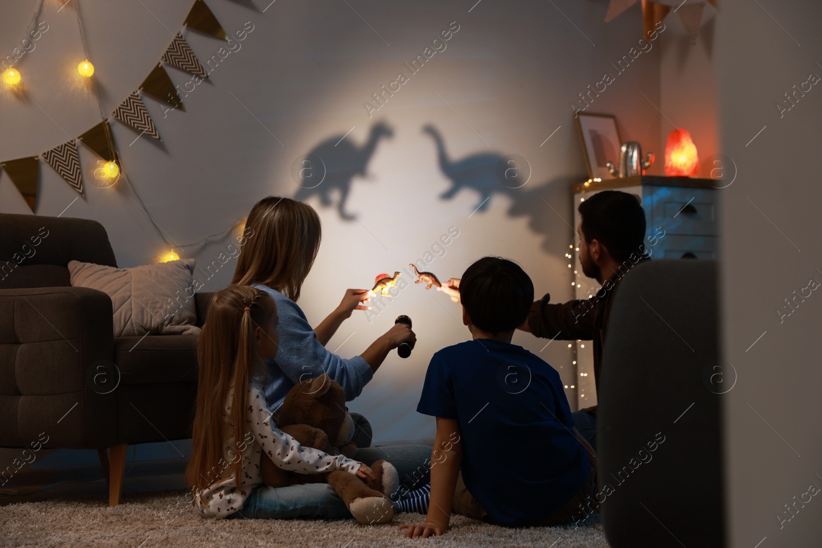 Photo of Parents performing shadow play with toy dinosaurs to their kids at home