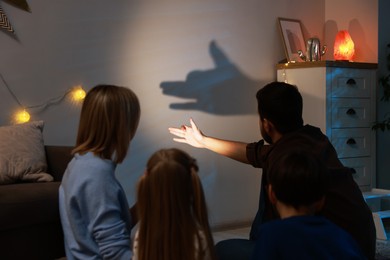 Photo of Man making hand gesture like dog while performing shadow play to his family at home, back view