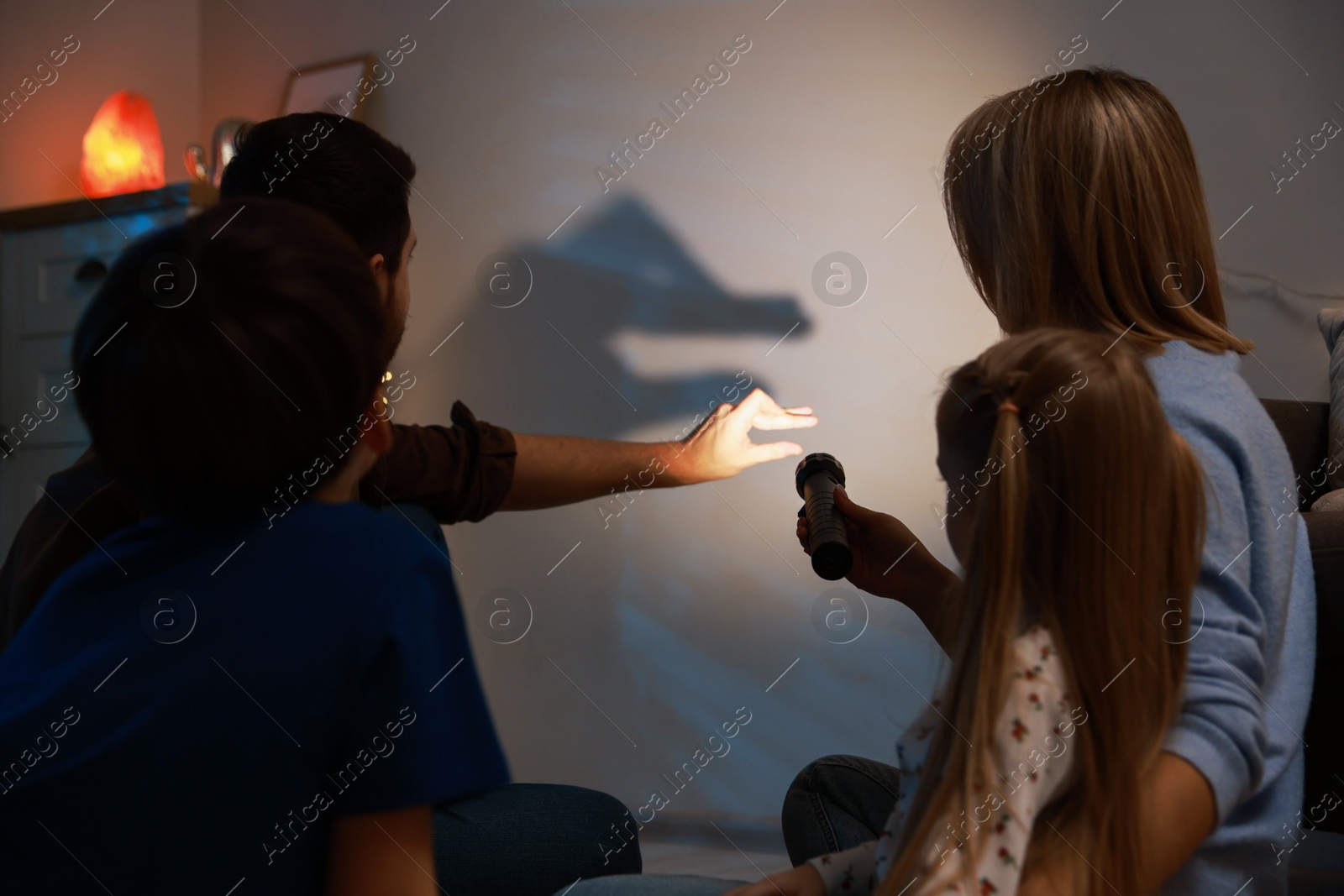 Photo of Man making hand gesture like goose while performing shadow play to his family at home, back view