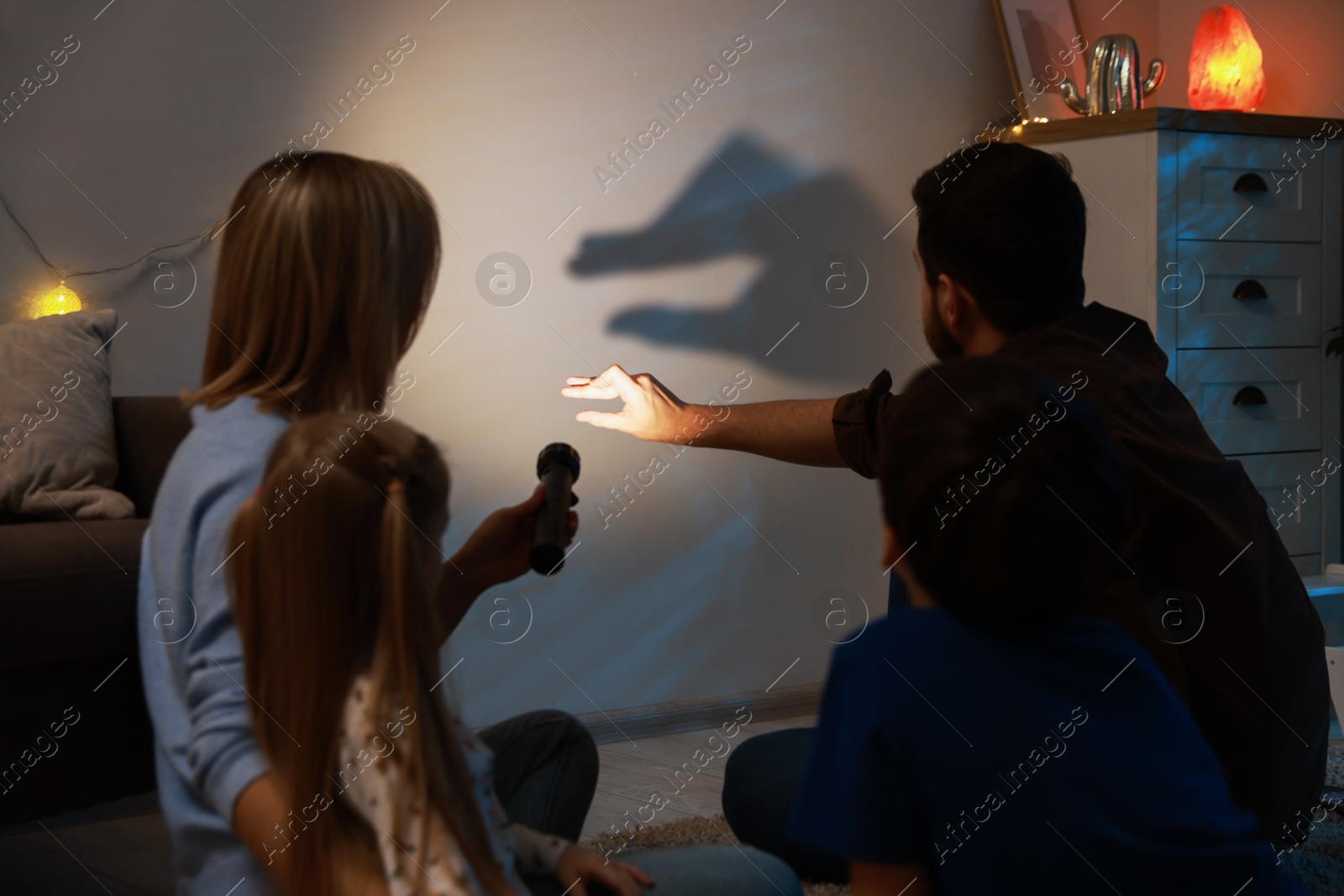 Photo of Man making hand gesture like goose while performing shadow play to his family at home, back view