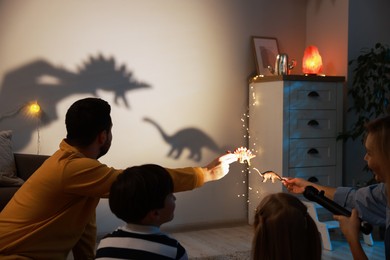 Photo of Parents performing shadow play with toy dinosaurs to their kids at home