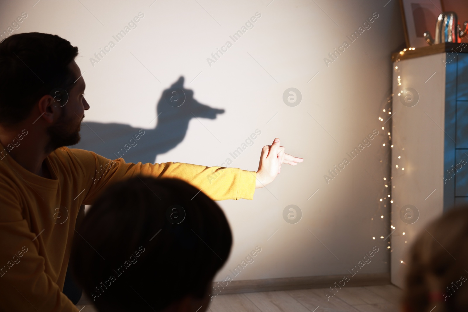 Photo of Man making hand gesture like llama while performing shadow play to his kids at home