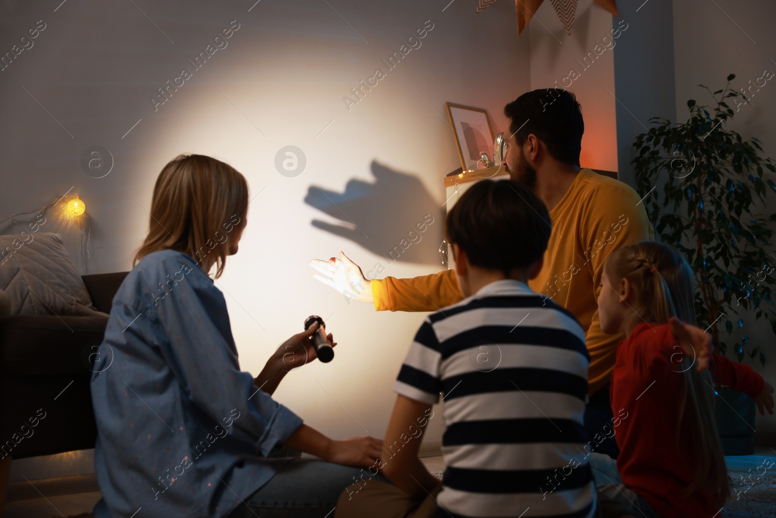 Photo of Man making hand gesture like dog while performing shadow play to his family at home