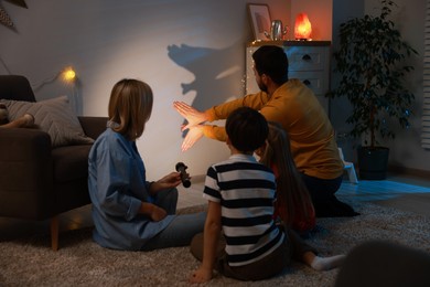 Photo of Man making hand gesture like bird while performing shadow play to his family at home