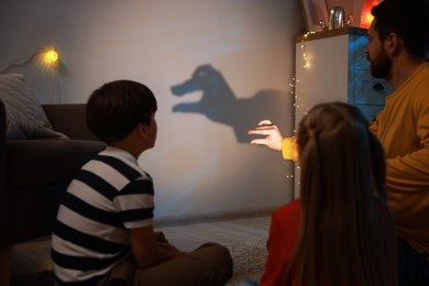 Photo of Man making hand gesture like goose while performing shadow play to his kids at home