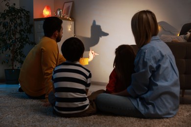 Photo of Man making hand gesture like llama while performing shadow play to his family at home, back view