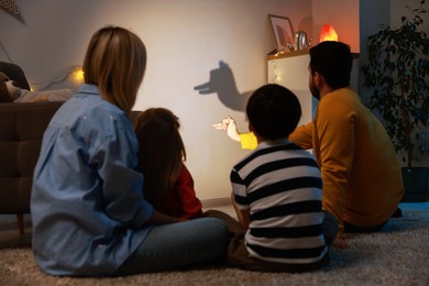 Photo of Man making hand gesture like llama while performing shadow play to his family at home, back view