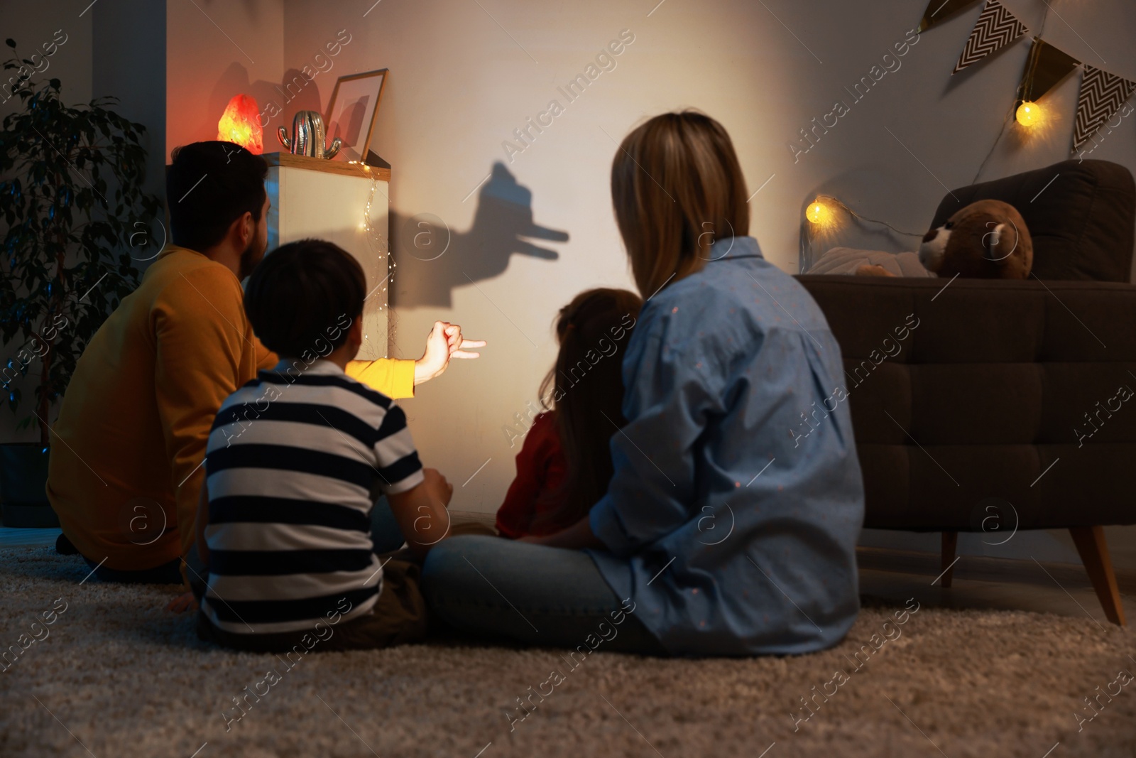 Photo of Man making hand gesture like llama while performing shadow play to his family at home, back view