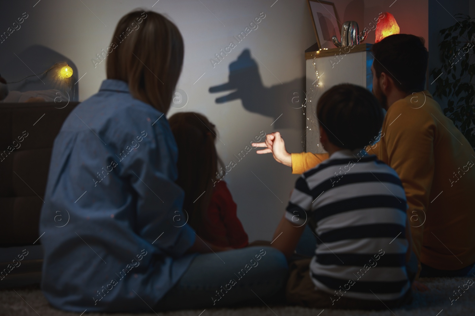 Photo of Man making hand gesture like llama while performing shadow play to his family at home, back view