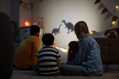 Photo of Parents performing shadow play with toy dinosaurs to their kids at home, back view