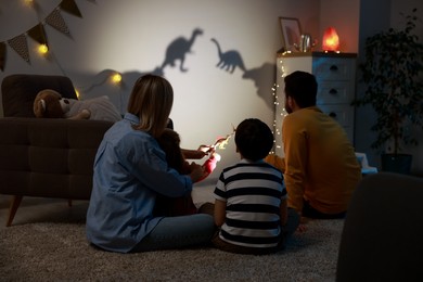 Photo of Parents performing shadow play with toy dinosaurs to their kids at home, back view