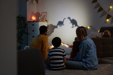 Photo of Parents performing shadow play with toy dinosaurs to their kids at home, back view