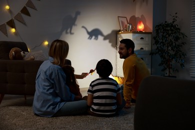 Photo of Parents performing shadow play with toy dinosaurs to their kids at home