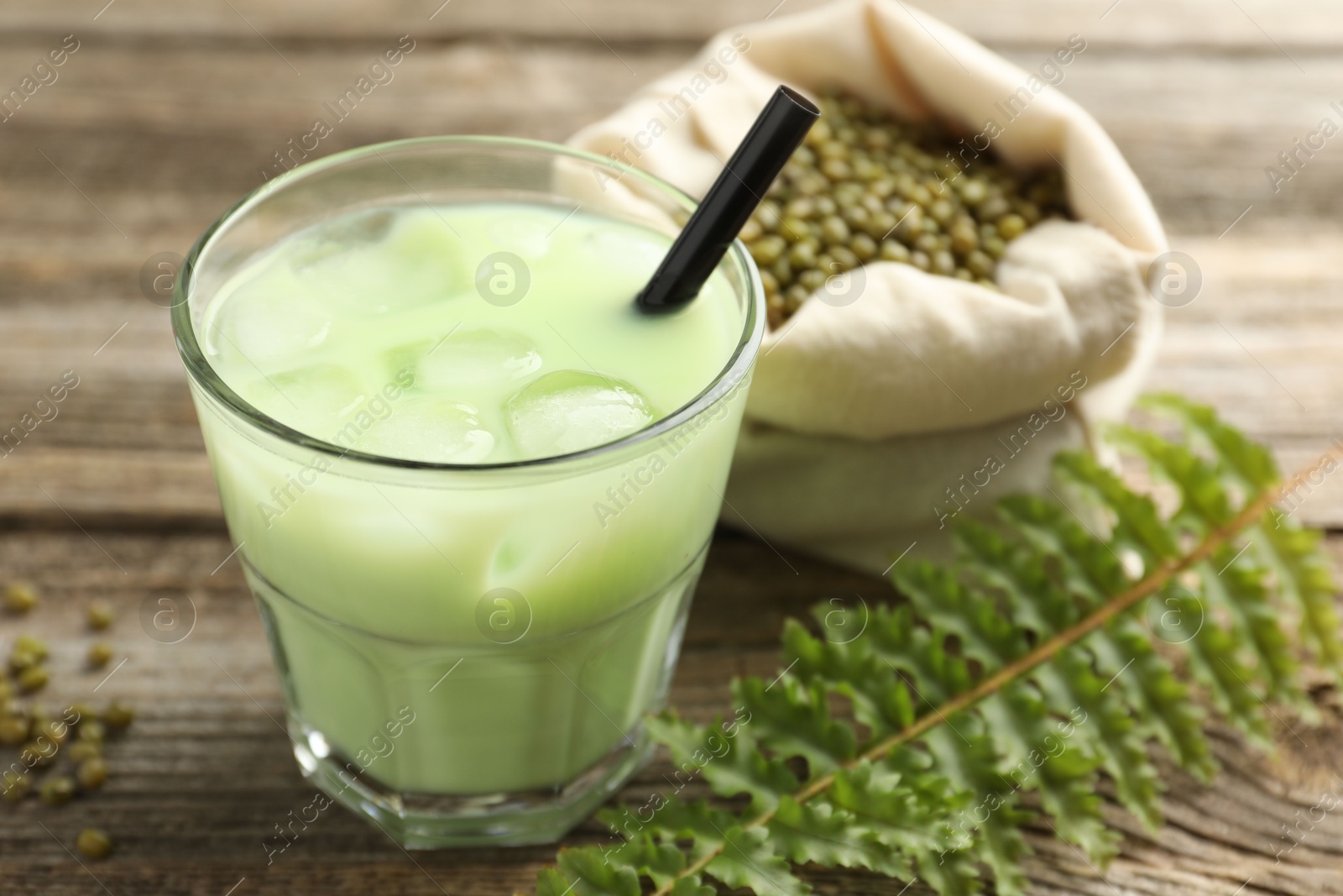 Fresh mung bean juice with ice in glass, leaves and seeds on wooden table, closeup Photo of Fresh mung bean juice with ice in glass, leaves and seeds on wooden table, closeup