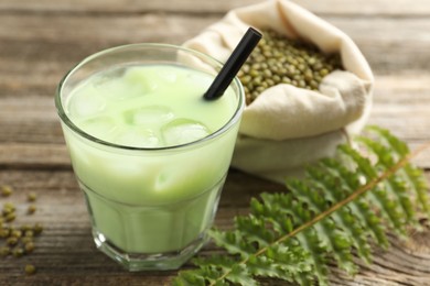 Photo of Fresh mung bean juice with ice in glass, leaves and seeds on wooden table, closeup