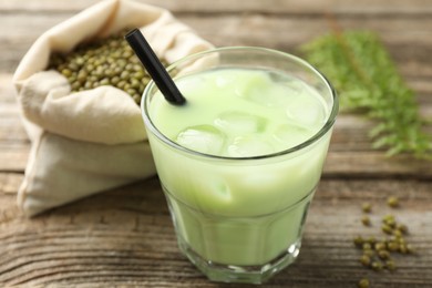 Photo of Fresh mung bean juice with ice in glass and seeds on wooden table, closeup
