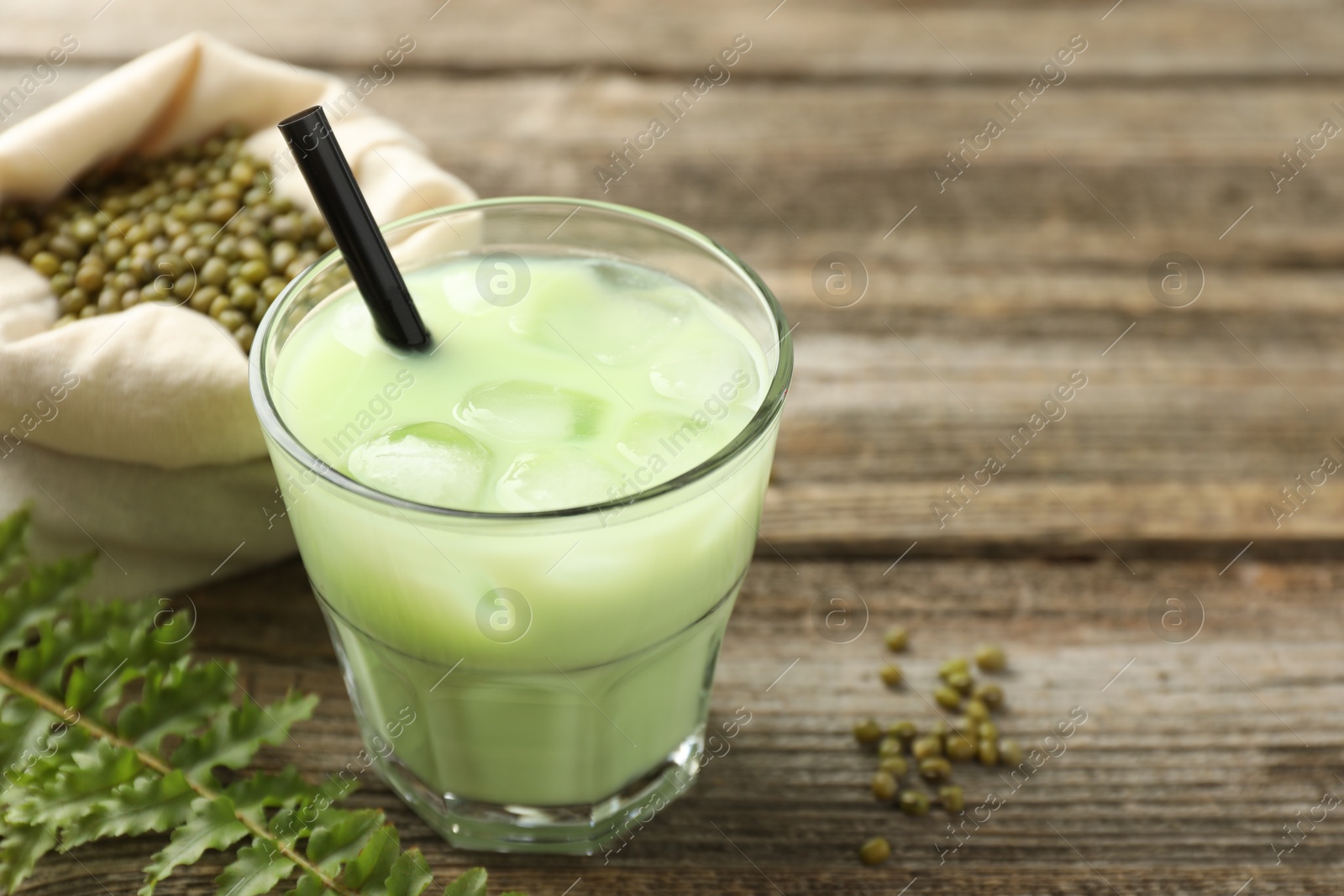 Fresh mung bean juice with ice in glass, leaves and seeds on wooden table, closeup. Space for text Photo of Fresh mung bean juice with ice in glass, leaves and seeds on wooden table, closeup. Space for text