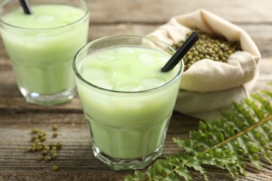 Photo of Fresh mung bean juice with ice in glasses, leaves and seeds on wooden table, closeup