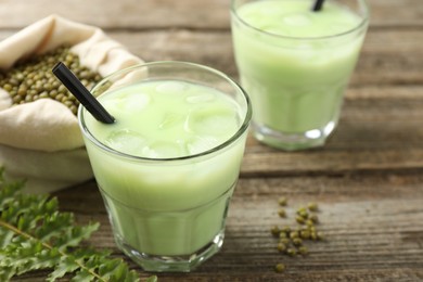 Photo of Fresh mung bean juice with ice in glasses, leaves and seeds on wooden table, closeup