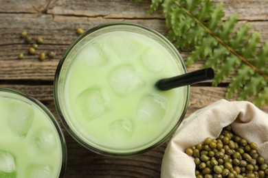 Photo of Fresh mung bean juice with ice in glasses, leaves and seeds on wooden table, flat lay