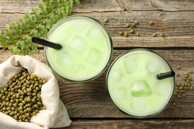 Photo of Fresh mung bean juice with ice in glasses, leaves and seeds on wooden table, flat lay