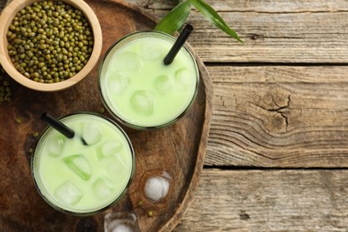 Photo of Fresh mung bean juice with ice in glasses and seeds on wooden table, flat lay. Space for text