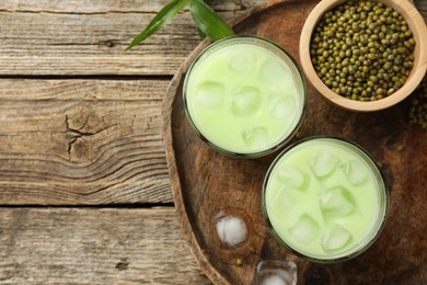 Photo of Fresh mung bean juice with ice in glasses and seeds on wooden table, flat lay. Space for text