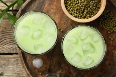 Photo of Fresh mung bean juice with ice in glasses and seeds on wooden table, flat lay