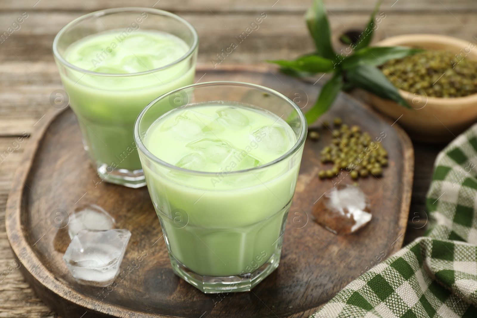 Fresh mung bean juice with ice in glasses and seeds on wooden table, closeup Photo of Fresh mung bean juice with ice in glasses and seeds on wooden table, closeup
