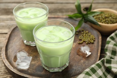 Photo of Fresh mung bean juice with ice in glasses and seeds on wooden table, closeup
