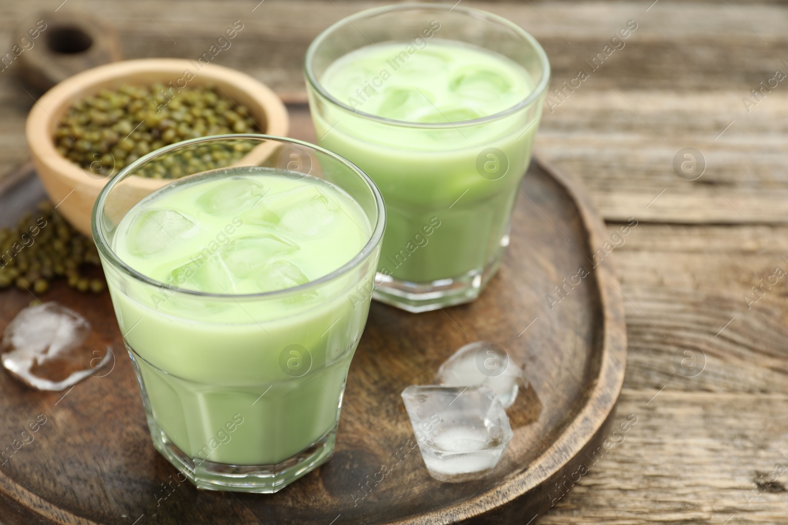 Photo of Fresh mung bean juice with ice in glasses and seeds on wooden table, closeup