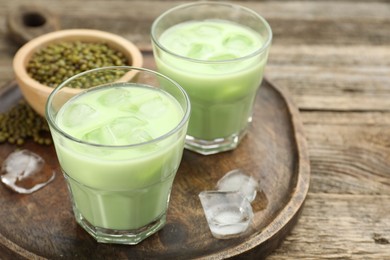 Photo of Fresh mung bean juice with ice in glasses and seeds on wooden table, closeup