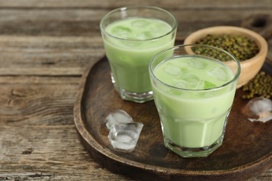 Photo of Fresh mung bean juice with ice in glasses and seeds on wooden table, closeup. Space for text