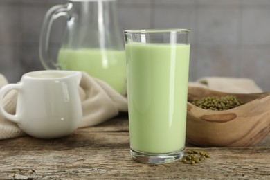 Photo of Fresh mung bean juice in glass and seeds on wooden table against grey tiled wall, closeup