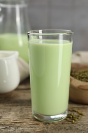 Photo of Fresh mung bean juice in glass and seeds on wooden table against grey wall, closeup