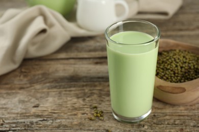 Photo of Fresh mung bean juice in glass and seeds on wooden table, closeup. Space for text