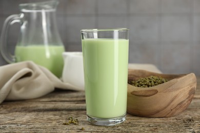 Photo of Fresh mung bean juice in glass and seeds on wooden table against grey tiled wall, closeup