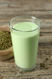 Photo of Fresh mung bean juice in glass and seeds on wooden table, closeup