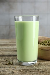 Photo of Fresh mung bean juice in glass and seeds on wooden table against grey wall, closeup